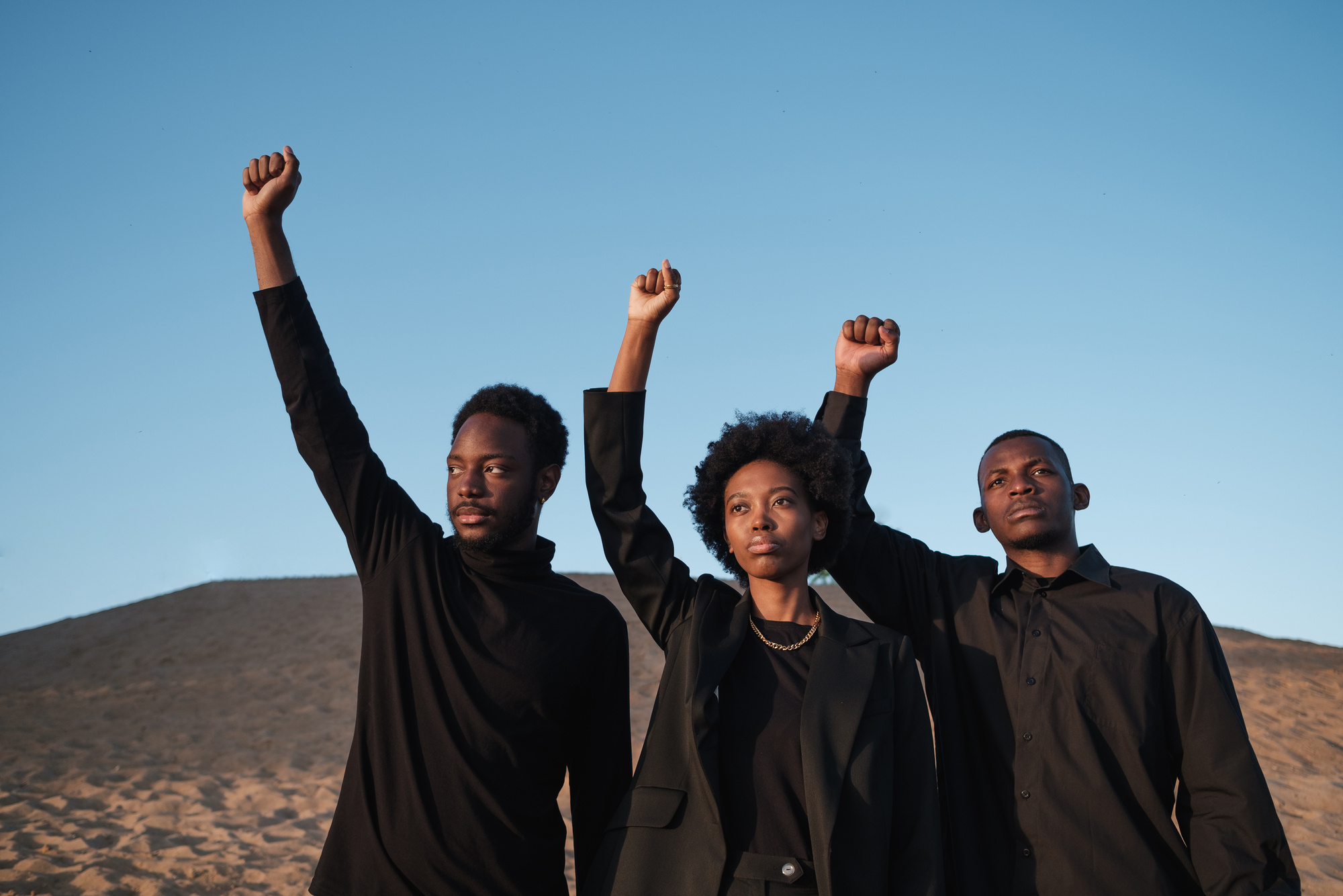 Three Diverse People in Black Outfit Raising Their Fist Outdoors